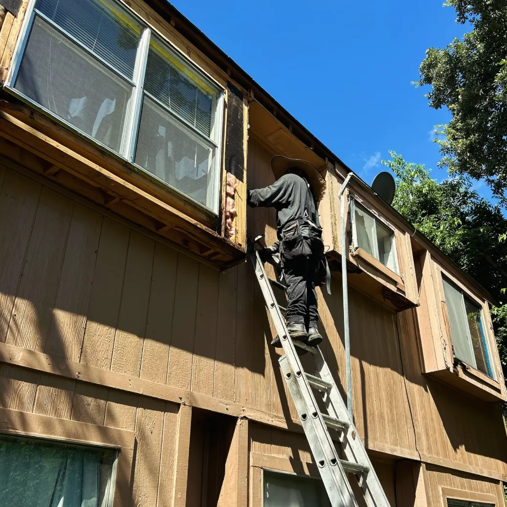 Barrantes crew member on a ladder replacing rotted window trim and siding